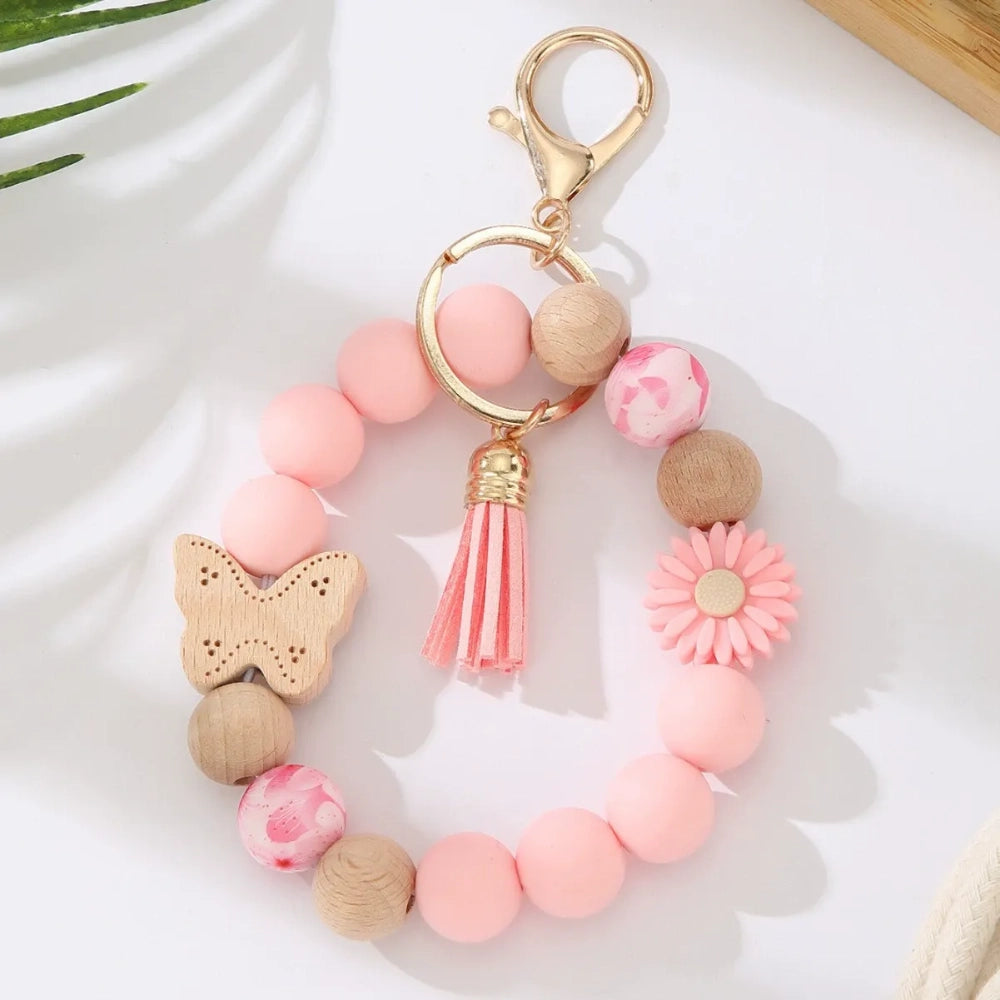 Assorted butterfly and flower silicone and wood bead keychain bracelets in pink, yellow, white, peach, black, purple, and green colorways with gold lobster clasp hardware and tassel accents for DIY jewelry making. - Pink