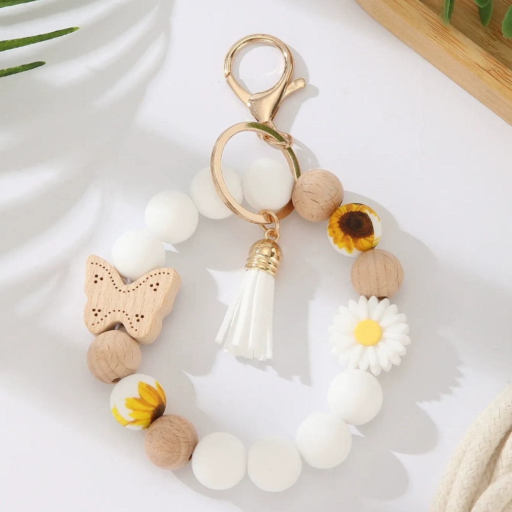Assorted butterfly and flower silicone and wood bead keychain bracelets in pink, yellow, white, peach, black, purple, and green colorways with gold lobster clasp hardware and tassel accents for DIY jewelry making. - White