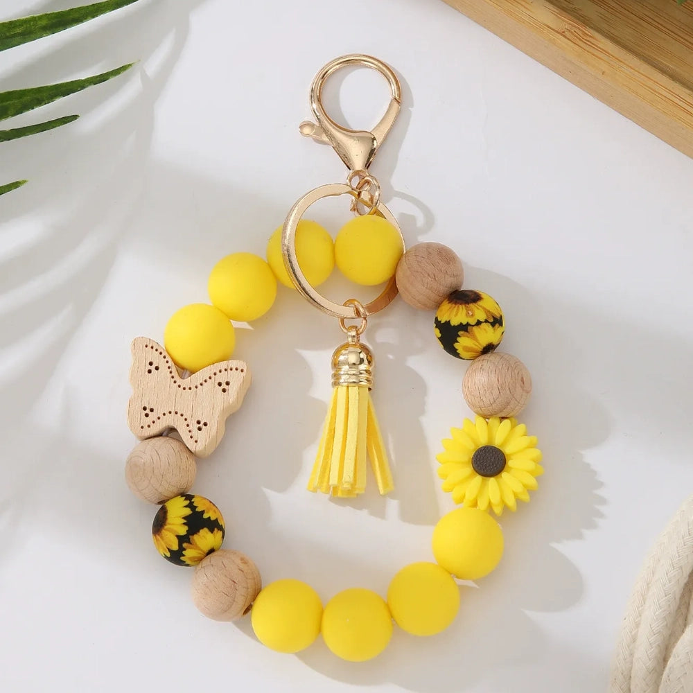 Assorted butterfly and flower silicone and wood bead keychain bracelets in pink, yellow, white, peach, black, purple, and green colorways with gold lobster clasp hardware and tassel accents for DIY jewelry making. - Yellow