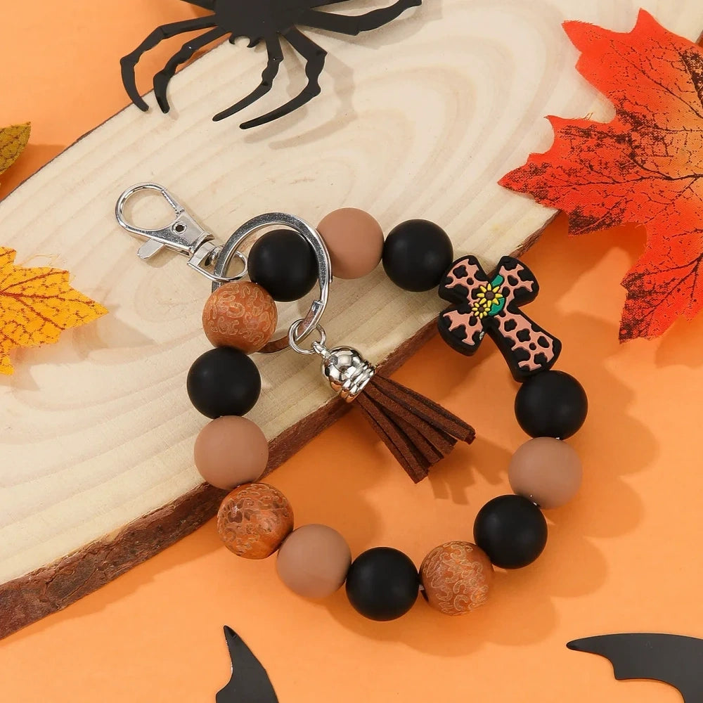 Assorted cactus charm silicone bead keychain bracelets in black, pink, mint, and white with leopard and cow print patterns, displayed on an orange Halloween-themed background. - Brown