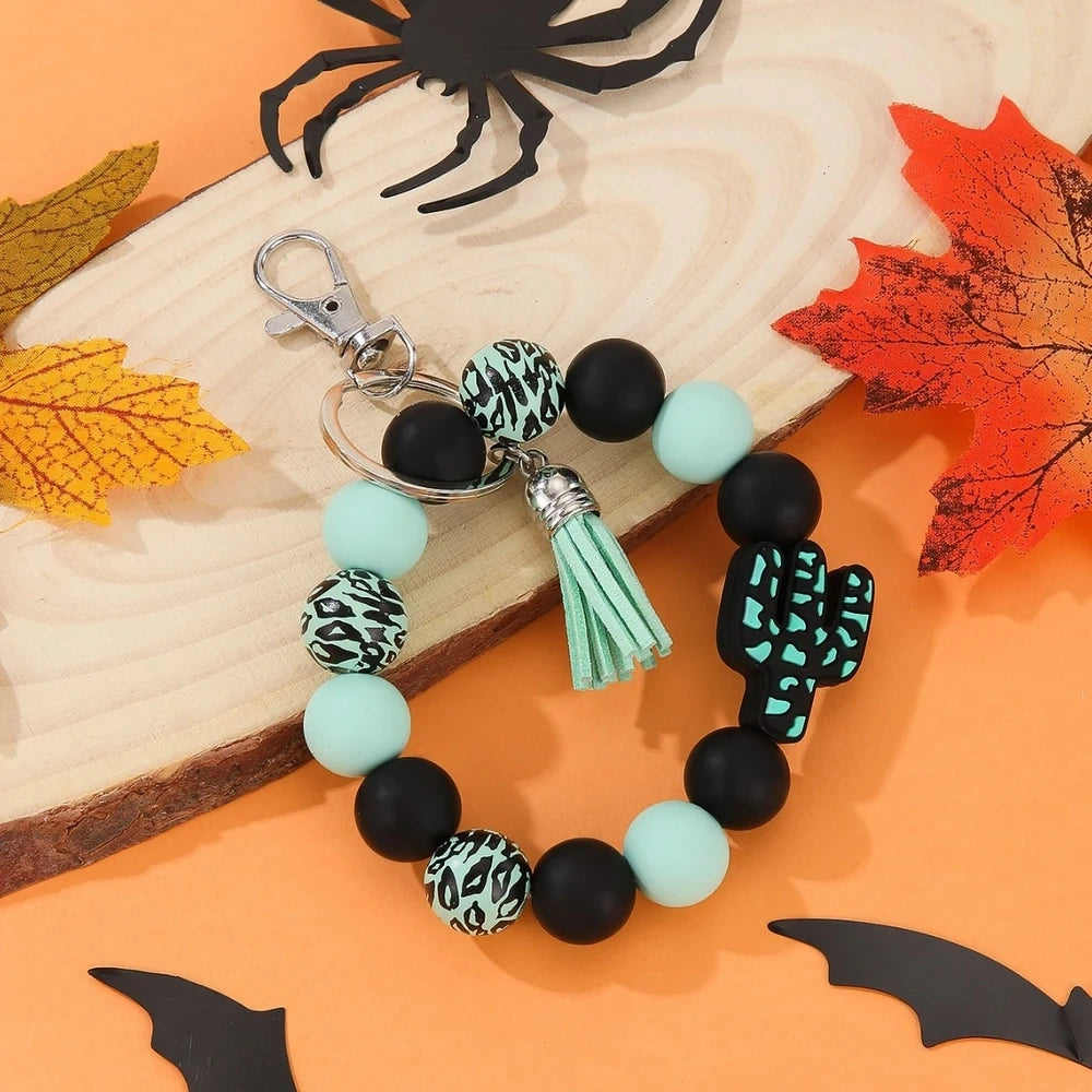 Assorted cactus charm silicone bead keychain bracelets in black, pink, mint, and white with leopard and cow print patterns, displayed on an orange Halloween-themed background. - Green