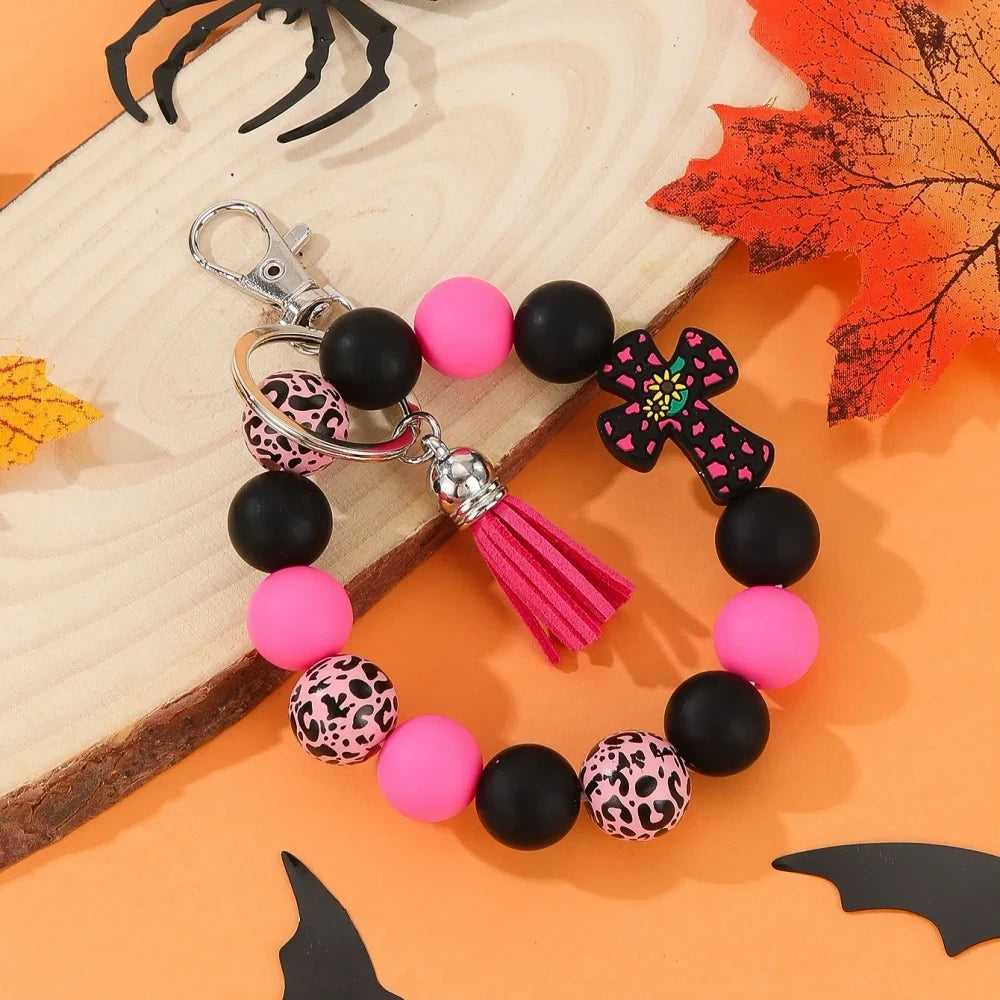 Assorted cactus charm silicone bead keychain bracelets in black, pink, mint, and white with leopard and cow print patterns, displayed on an orange Halloween-themed background. - Rose Red