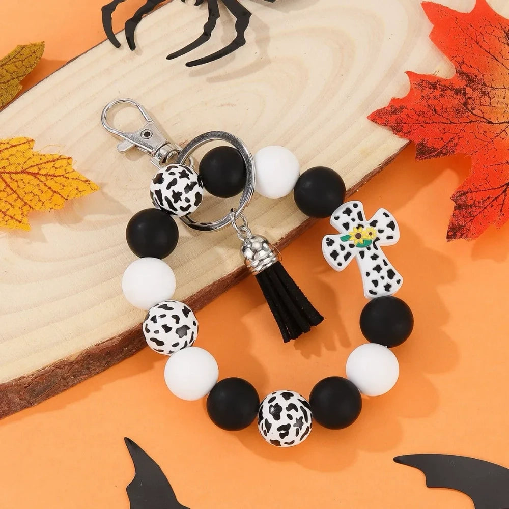 Assorted cactus charm silicone bead keychain bracelets in black, pink, mint, and white with leopard and cow print patterns, displayed on an orange Halloween-themed background. - White