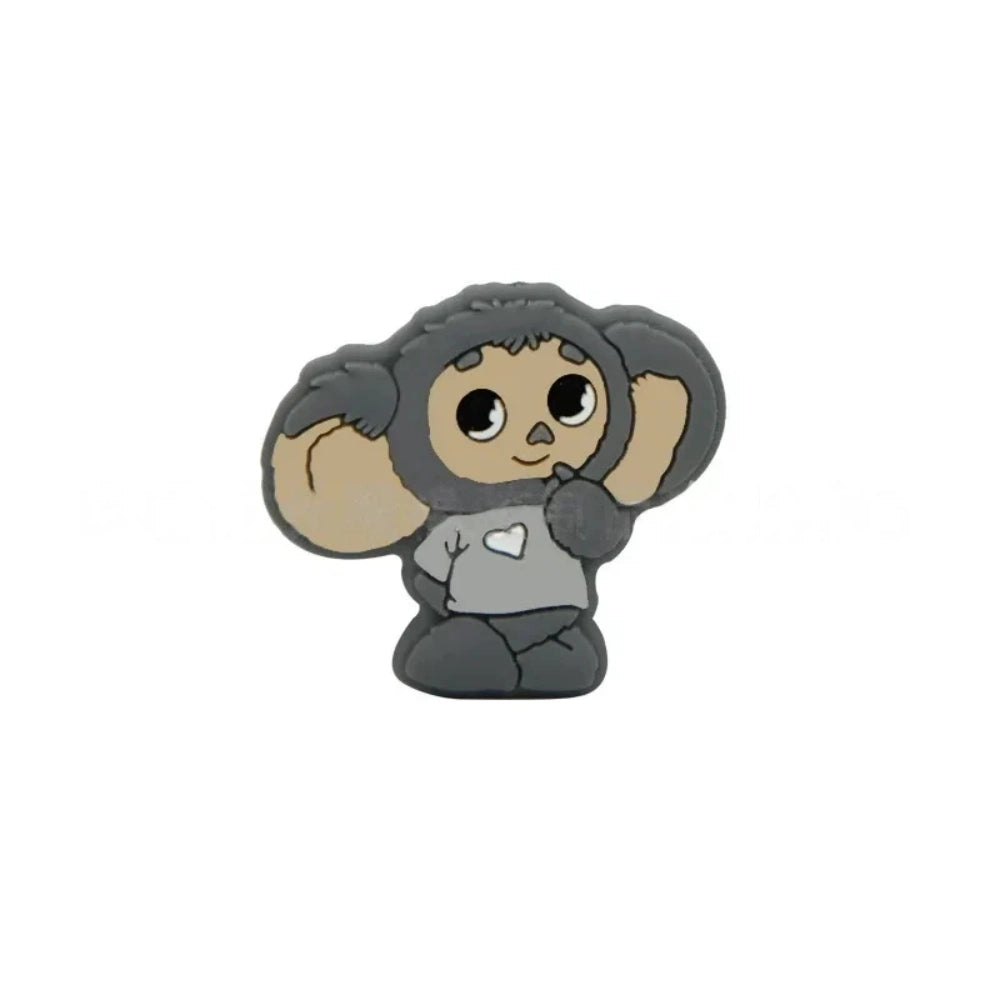 Four Cheburashka silicone focal beads in blue, red, gray, and pink colorways displayed on beadable pens against a pink background. - Dark Gray