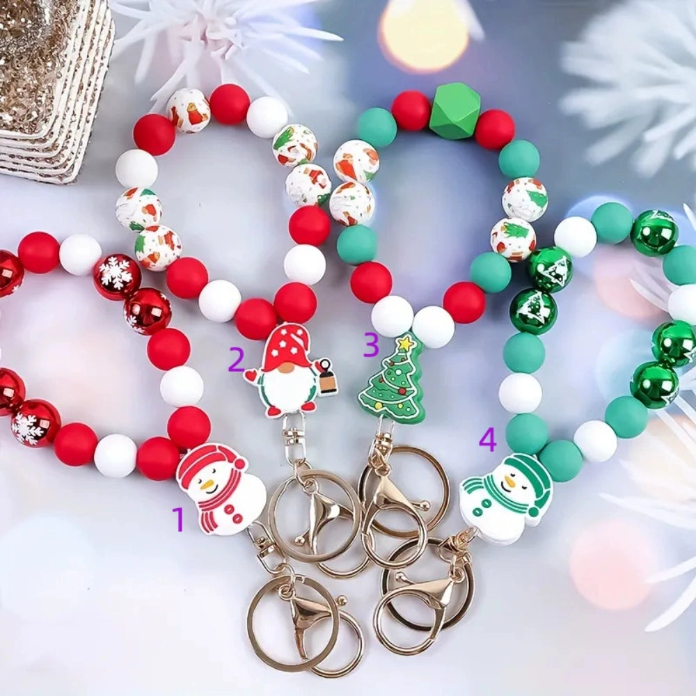 Four Christmas silicone bead bracelet keychains in red and green colorways featuring snowman, gnome, and Christmas tree charms with gold lobster clasp and key rings on a festive background.