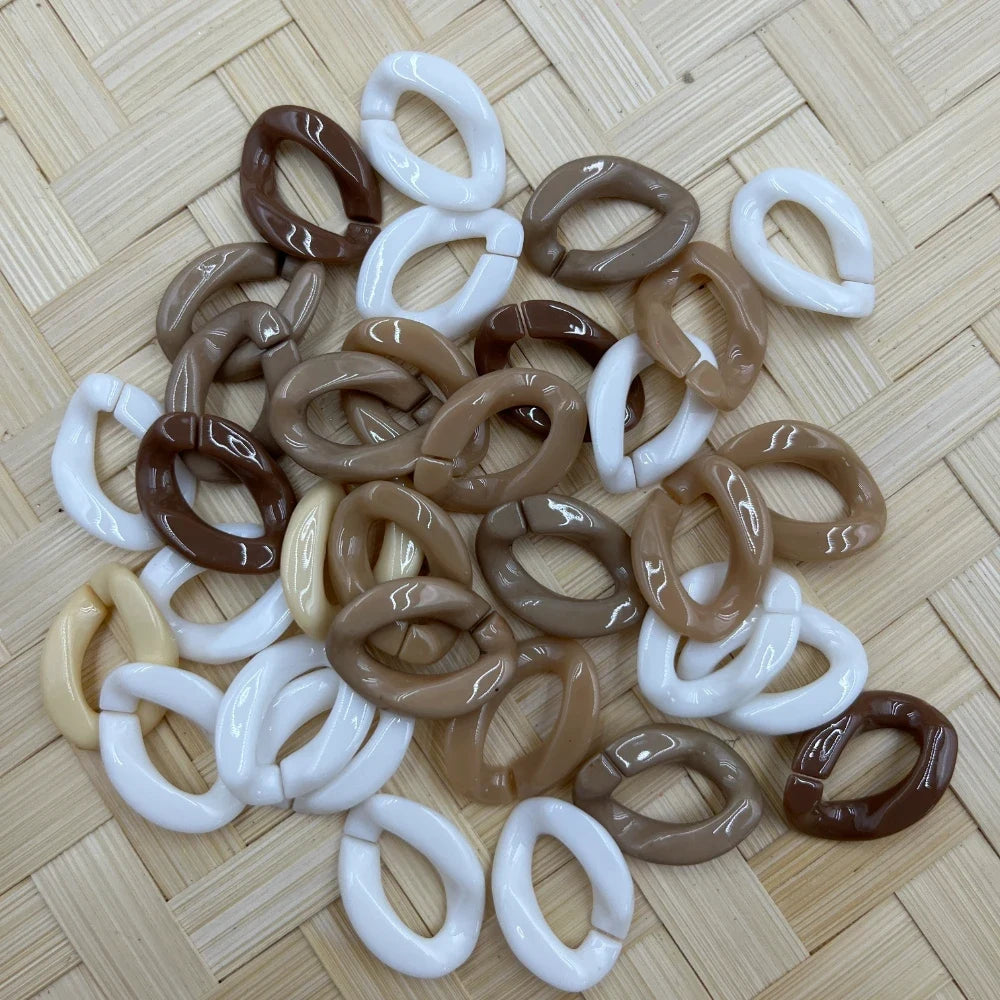 Glossy chunky oval chain link acrylic beads in neutral tones including white, brown, tan, and cream, scattered on a woven bamboo surface for DIY jewelry making and beadable pens.
