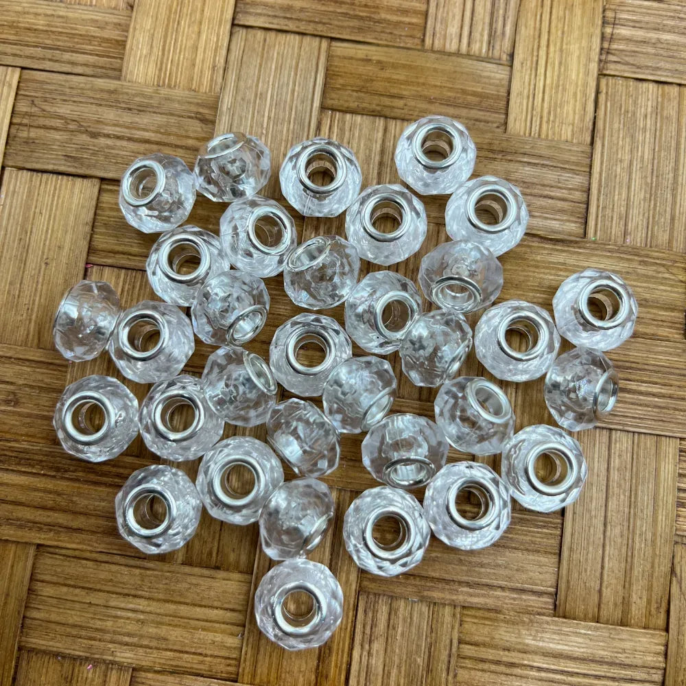 Clear crystal faceted acrylic spacer beads with silver metal core holes, arranged on a woven bamboo surface, ideal for beadable pens, bracelets, and DIY jewelry making.