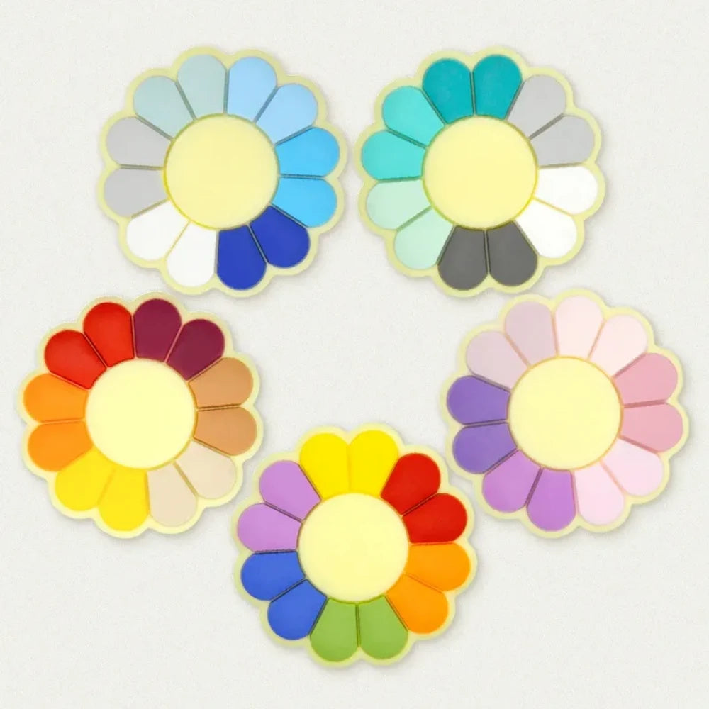 Five color wheel flower silicone focal beads arranged in a circle, each featuring a yellow center with multicolored petals in cool blues, teals, warm reds, pastels, and rainbow combinations on a light gray background.