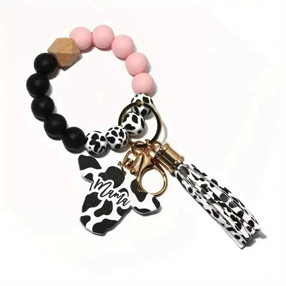 Cow print black and white silicone beads mixed with solid color silicone beads on bracelet keychains with mama butterfly charm and tassel pendants in pink, black, teal, and purple color combinations - Pink