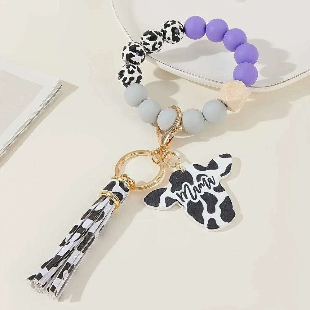 Cow print black and white silicone beads mixed with solid color silicone beads on bracelet keychains with mama butterfly charm and tassel pendants in pink, black, teal, and purple color combinations - Purple
