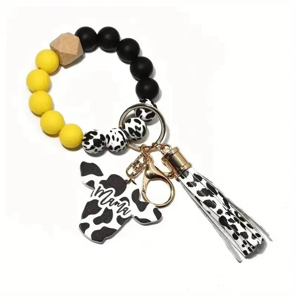Cow print black and white silicone beads mixed with solid color silicone beads on bracelet keychains with mama butterfly charm and tassel pendants in pink, black, teal, and purple color combinations - Yellow