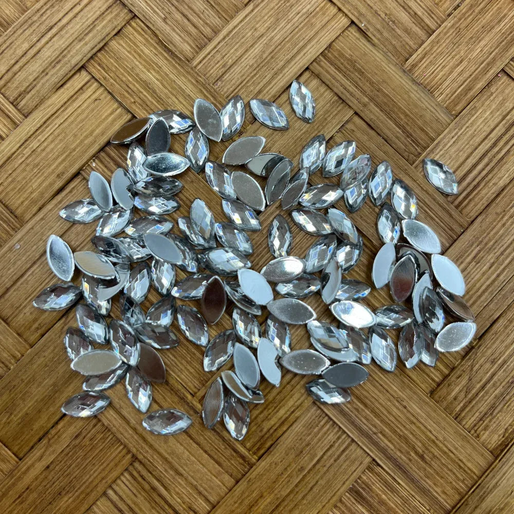 Loose crystal clear navette marquise flatback rhinestones with silver foil backing scattered on a wicker surface, ideal for DIY jewelry making and craft embellishments.