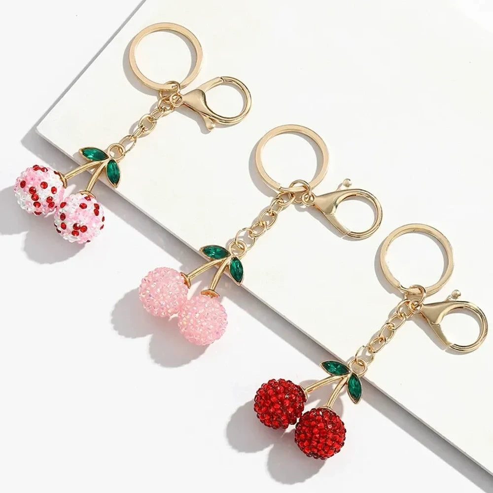 Three crystal rhinestone cherry charm keychains in pink mixed, solid pink, and red, with gold tone stems and green leaf accents on a white background.