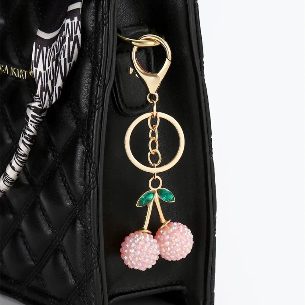 Three crystal rhinestone cherry charm keychains in pink mixed, solid pink, and red, with gold tone stems and green leaf accents on a white background. - Pink