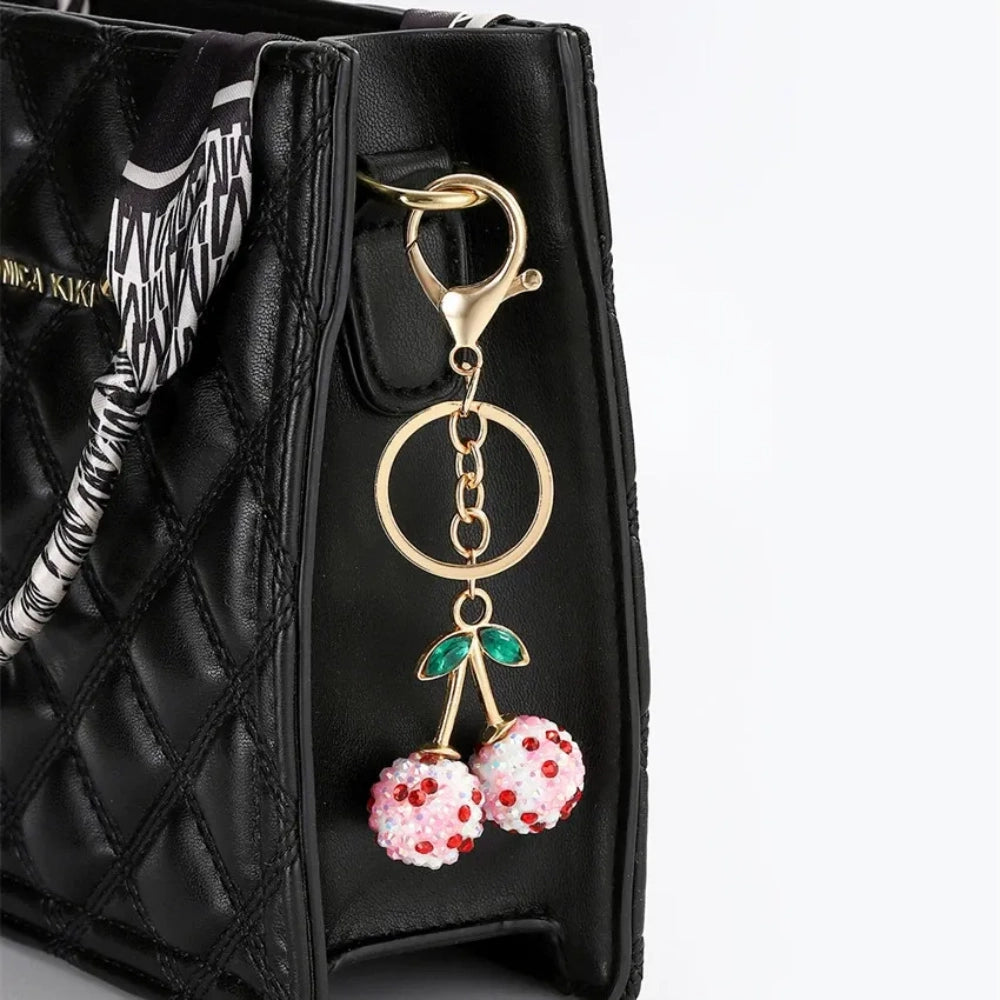 Three crystal rhinestone cherry charm keychains in pink mixed, solid pink, and red, with gold tone stems and green leaf accents on a white background. - Red-Pink