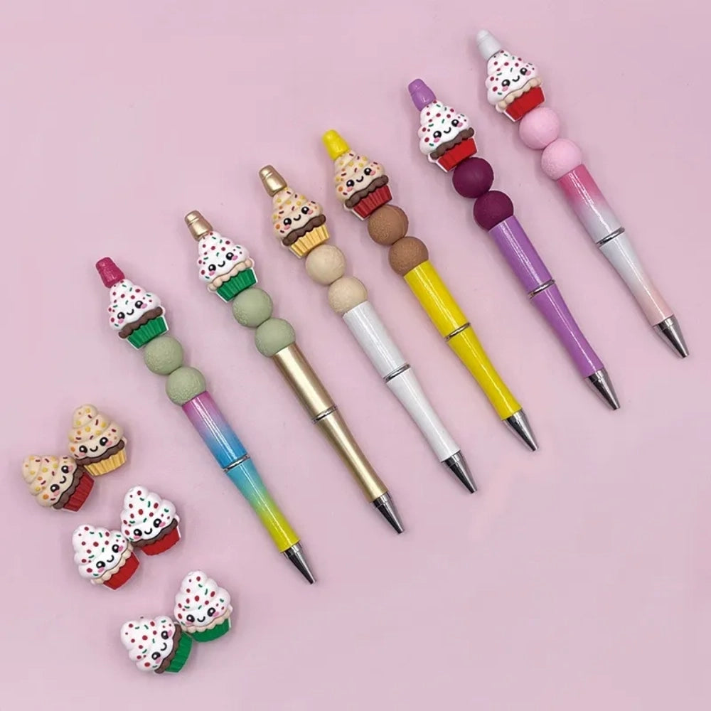 Assorted kawaii cupcake silicone focal beads with sprinkles and smiley faces shown on colorful beadable pens on a pink background, available at DIY Mini Planet.