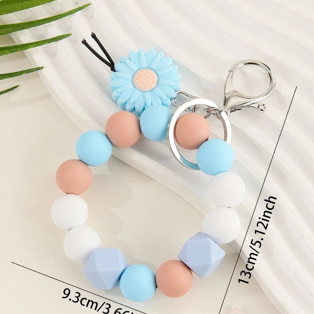 Seven colorful silicone bead keychain bracelet rings with daisy flower charms in various color combinations including orange, blue, yellow, green, purple, gray and brown on a white surface. - Blue