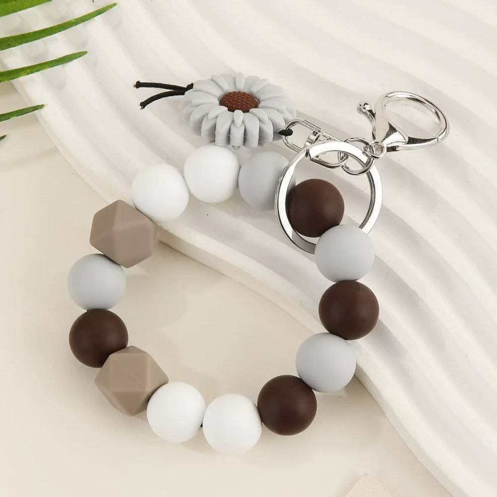 Seven colorful silicone bead keychain bracelet rings with daisy flower charms in various color combinations including orange, blue, yellow, green, purple, gray and brown on a white surface. - Gray