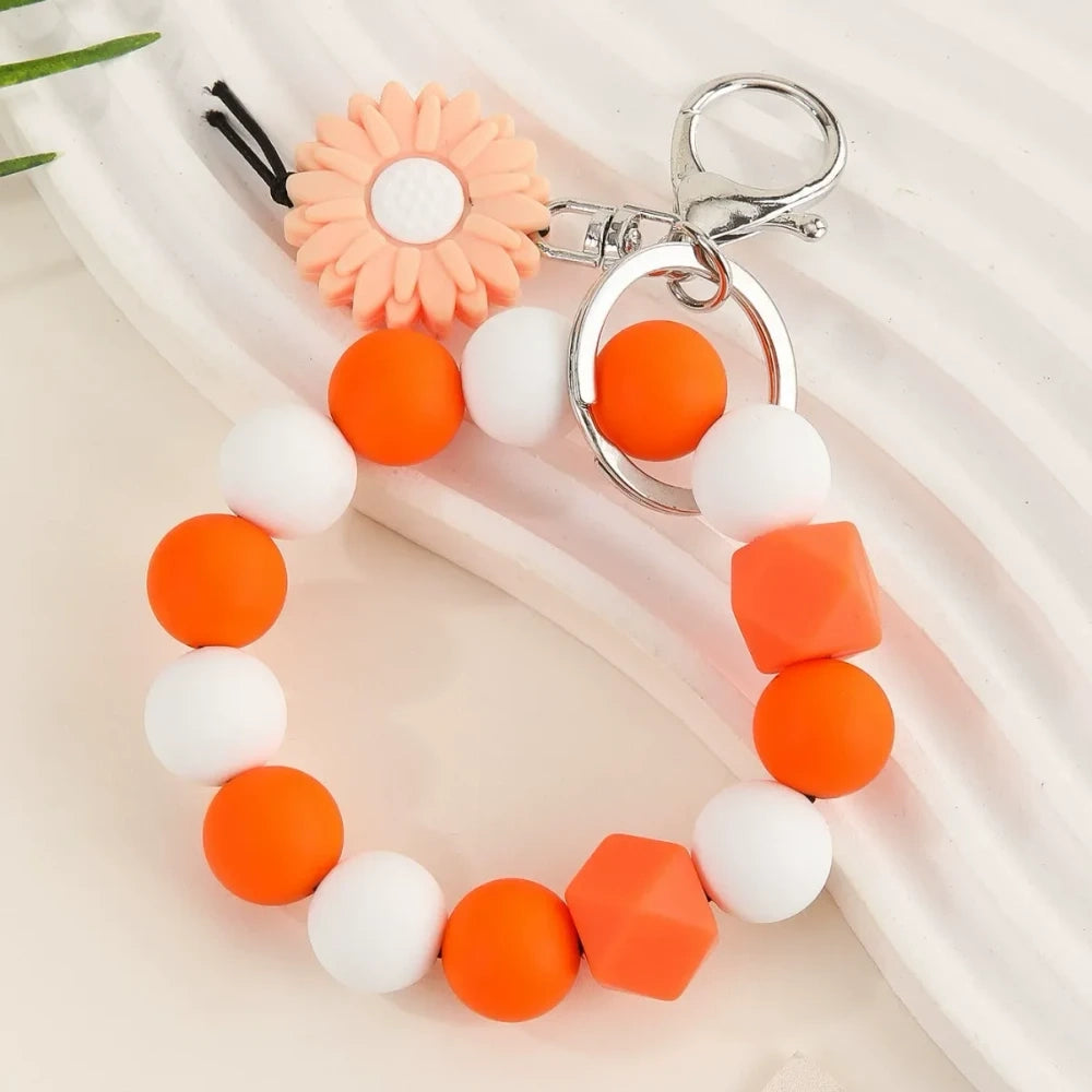Seven colorful silicone bead keychain bracelet rings with daisy flower charms in various color combinations including orange, blue, yellow, green, purple, gray and brown on a white surface. - Orange
