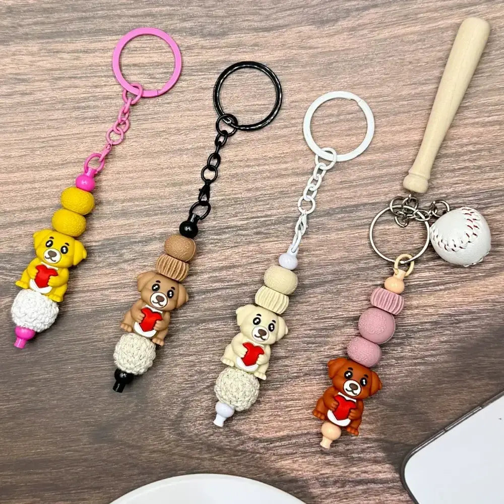 Four colorful dog holding heart 3D silicone focal beads in yellow, brown, cream, and dark brown shown on keychains with wood beads on a wooden surface.