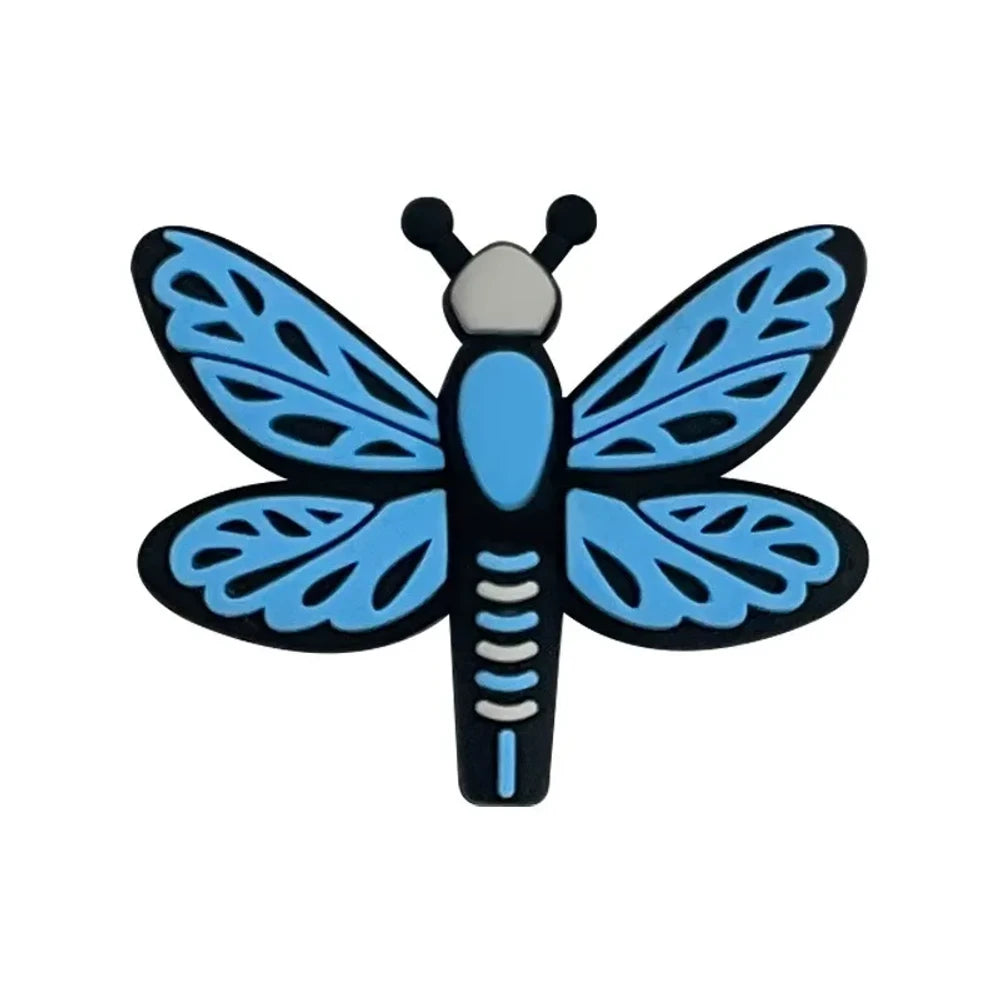 Seven colorful dragonfly silicone focal beads in pink, hot pink, light blue, and teal arranged on a pink background, featuring lace-pattern wings and black outlines. - Blue