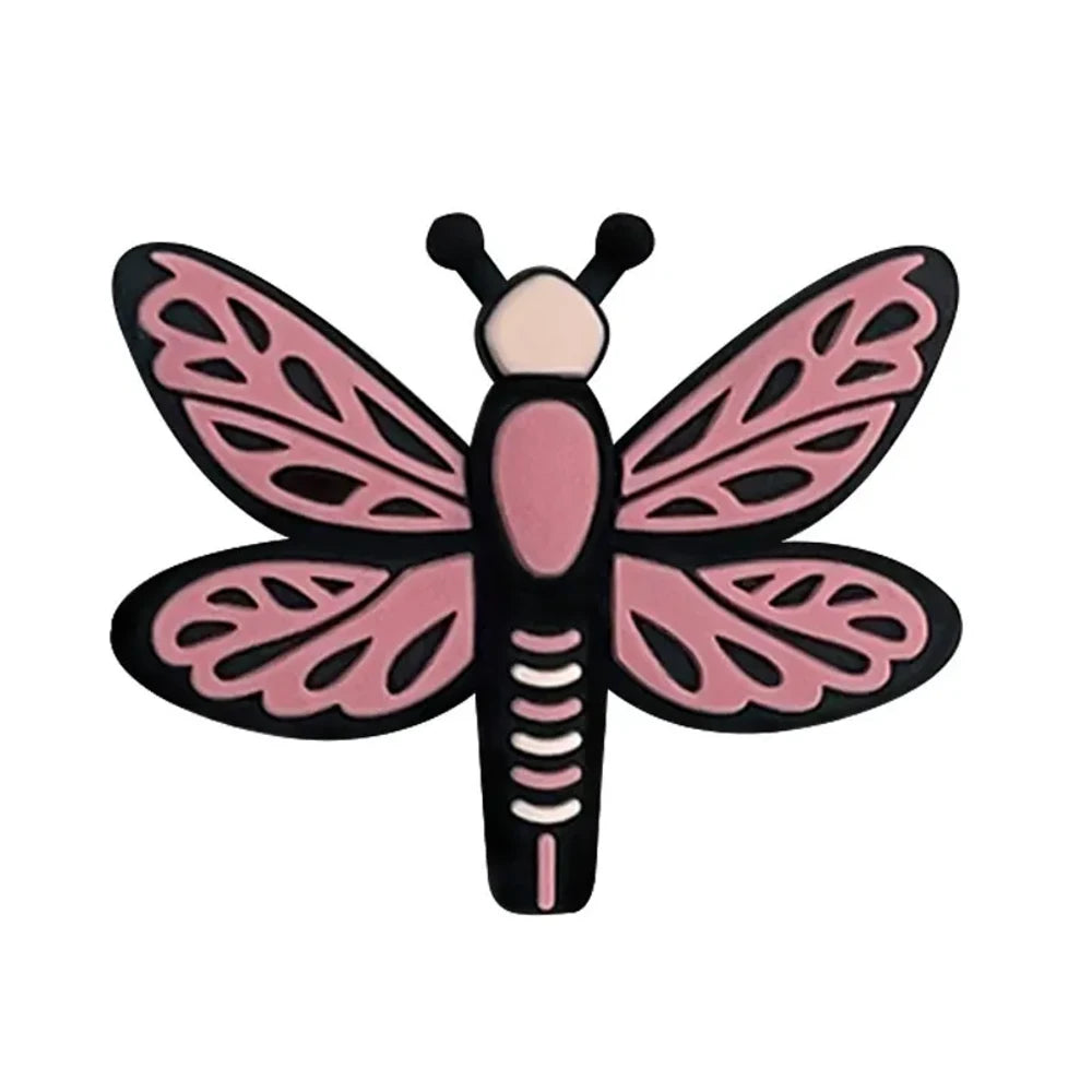 Seven colorful dragonfly silicone focal beads in pink, hot pink, light blue, and teal arranged on a pink background, featuring lace-pattern wings and black outlines. - Pink