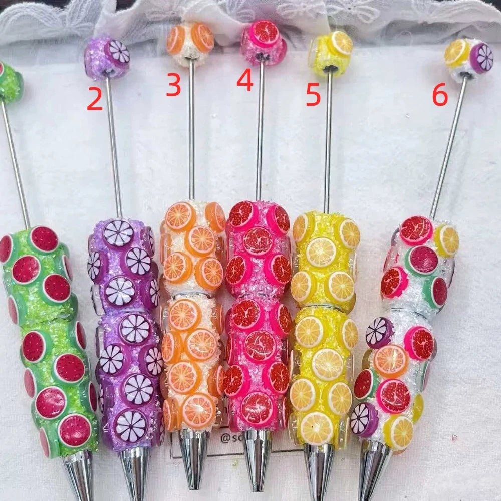 Six colorful fruit slice rhinestone beadable pens in green watermelon, purple citrus, orange, hot pink, yellow lemon, and mixed fruit designs with glitter resin handles and silver tips.