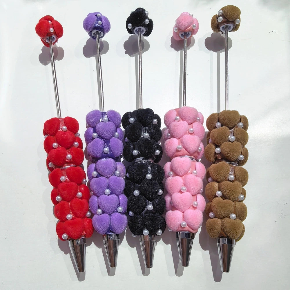 Five fuzzy heart plush beadable pens in red, purple, black, pink, and brown with pearl bead accents and silver metal tips, displayed on a white background.