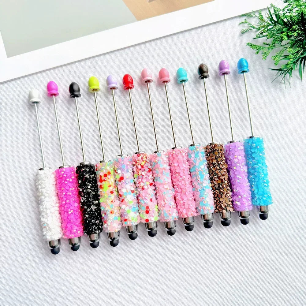 Set of 11 glitter rhinestone beadable pens in assorted colors including white, hot pink, black, multicolor, pink, light pink, teal, brown, purple, blue, and lavender, displayed on a white surface.
