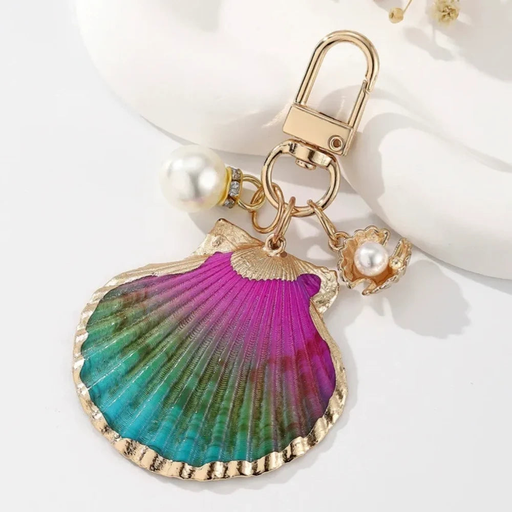 Four decorative shell keychain charms featuring leopard print, rainbow gradient, and natural orange shell designs with pearl beads and gold-tone metal hardware on a white background. - 1
