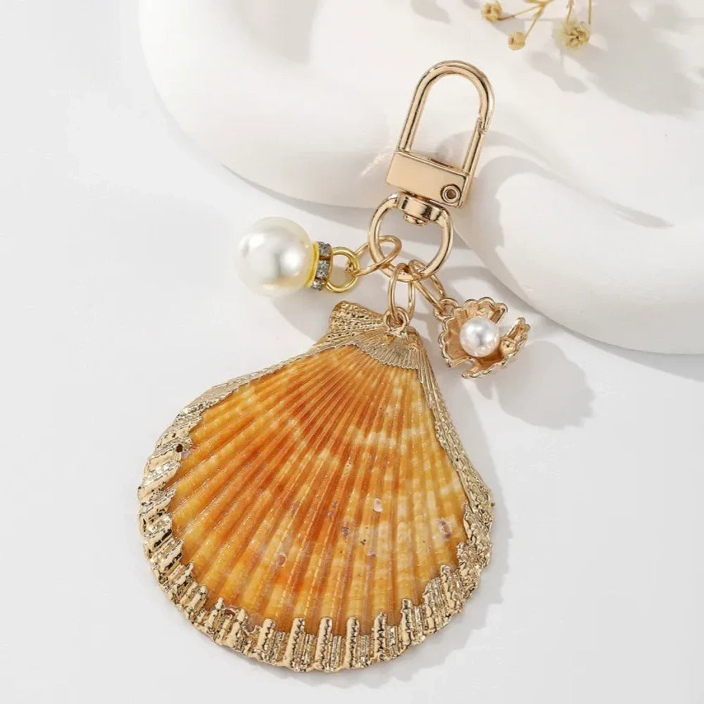 Four decorative shell keychain charms featuring leopard print, rainbow gradient, and natural orange shell designs with pearl beads and gold-tone metal hardware on a white background. - 3