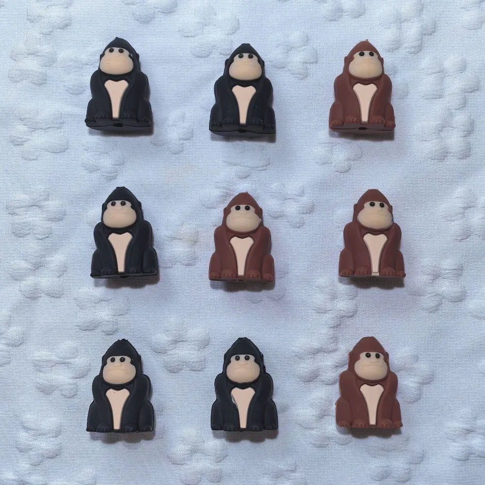 Nine 3D gorilla silicone focal beads arranged in a 3x3 grid, showing black and brown colorways of cartoon ape character beads on a white textured background.