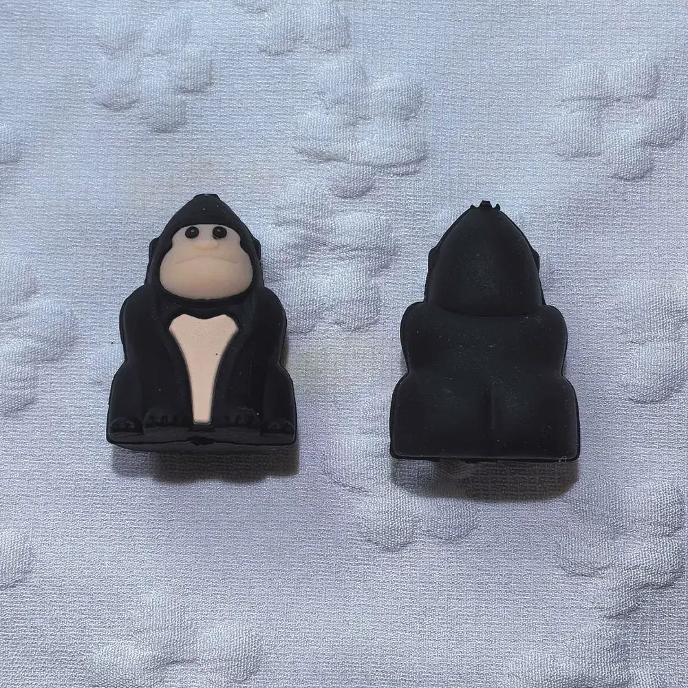 Nine 3D gorilla silicone focal beads arranged in a 3x3 grid, showing black and brown colorways of cartoon ape character beads on a white textured background. - Black