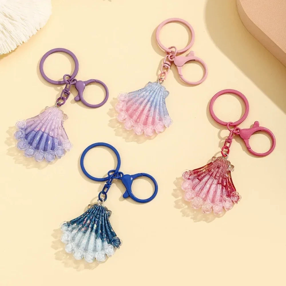 Four gradient glitter seashell resin keychain charms in purple, pink, blue, and red on a yellow background, featuring lobster clasp rings for DIY jewelry making and keychains.