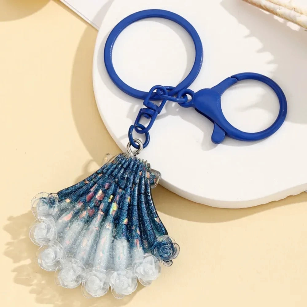 Four gradient glitter seashell resin keychain charms in purple, pink, blue, and red on a yellow background, featuring lobster clasp rings for DIY jewelry making and keychains. - 1