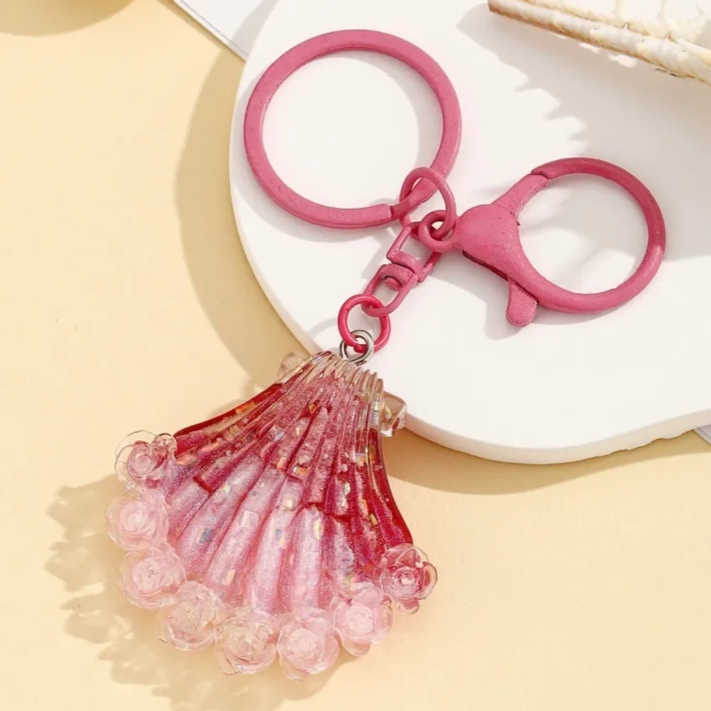 Four gradient glitter seashell resin keychain charms in purple, pink, blue, and red on a yellow background, featuring lobster clasp rings for DIY jewelry making and keychains. - 2