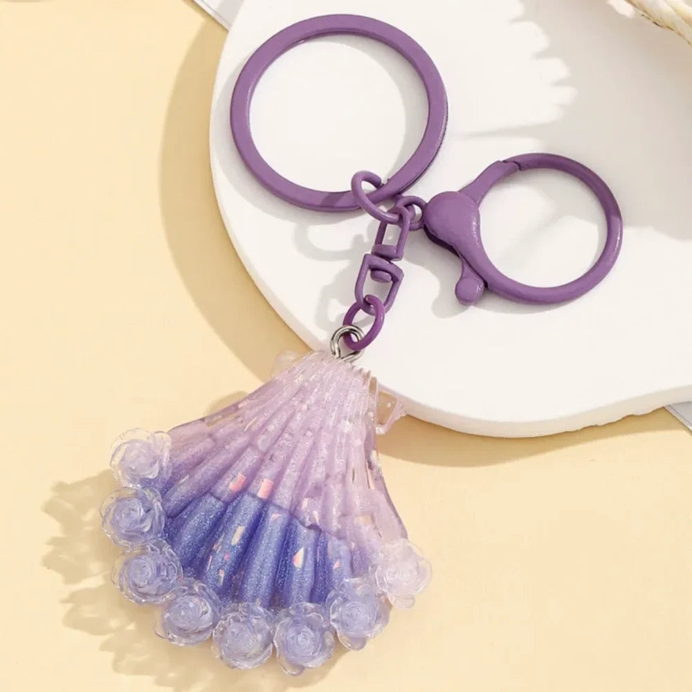Four gradient glitter seashell resin keychain charms in purple, pink, blue, and red on a yellow background, featuring lobster clasp rings for DIY jewelry making and keychains. - 3