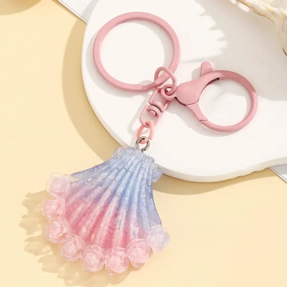 Four gradient glitter seashell resin keychain charms in purple, pink, blue, and red on a yellow background, featuring lobster clasp rings for DIY jewelry making and keychains. - 4
