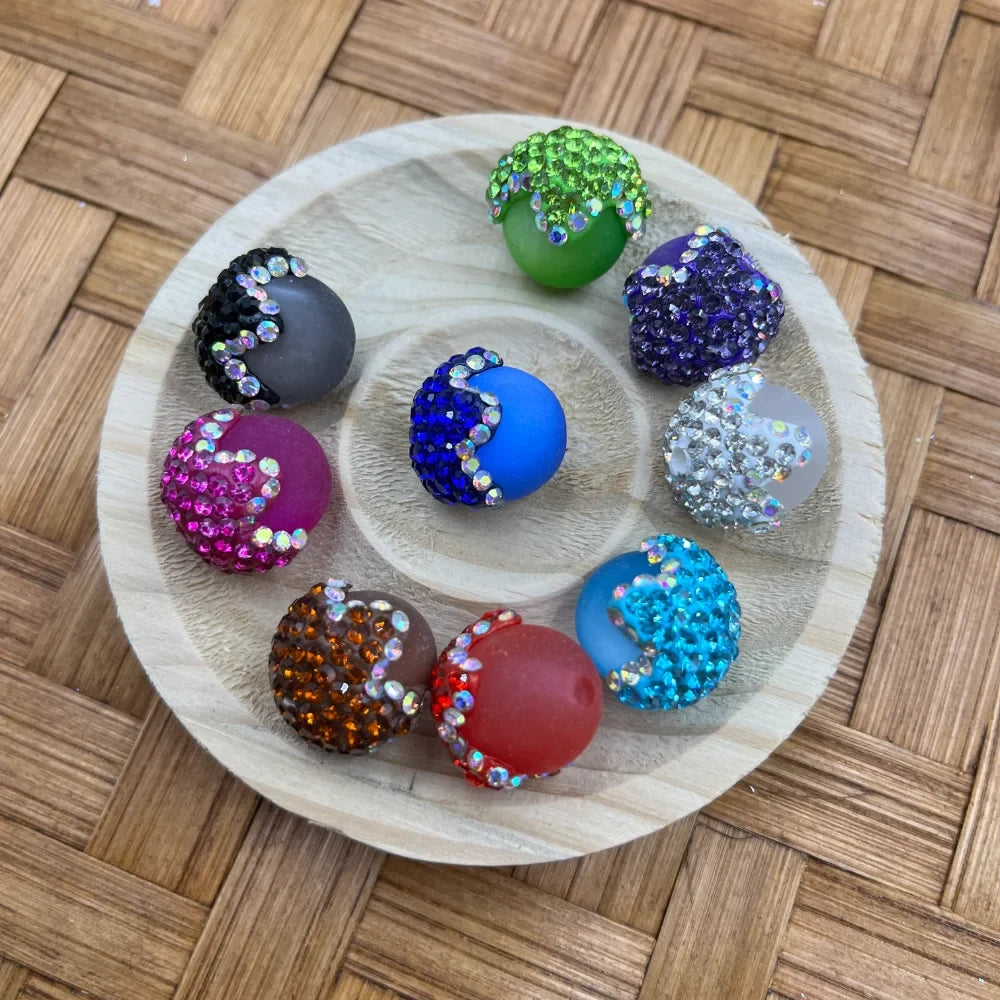 Ten colorful half rhinestone half matte silicone round beads in assorted colors including green, purple, blue, pink, teal, red, brown, gray, white, and black displayed on a round wooden tray on a wicker surface.