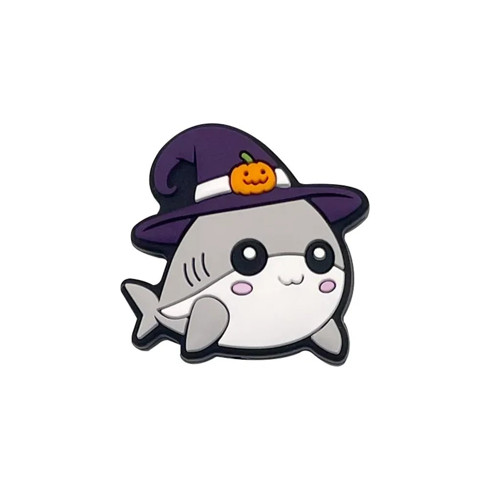 Cute Halloween silicone focal beads featuring ghost characters in orange knit hats with pumpkin balloons and shark characters in purple witch hats with jack-o-lantern accents, displayed on a miniature white bench. - Shark
