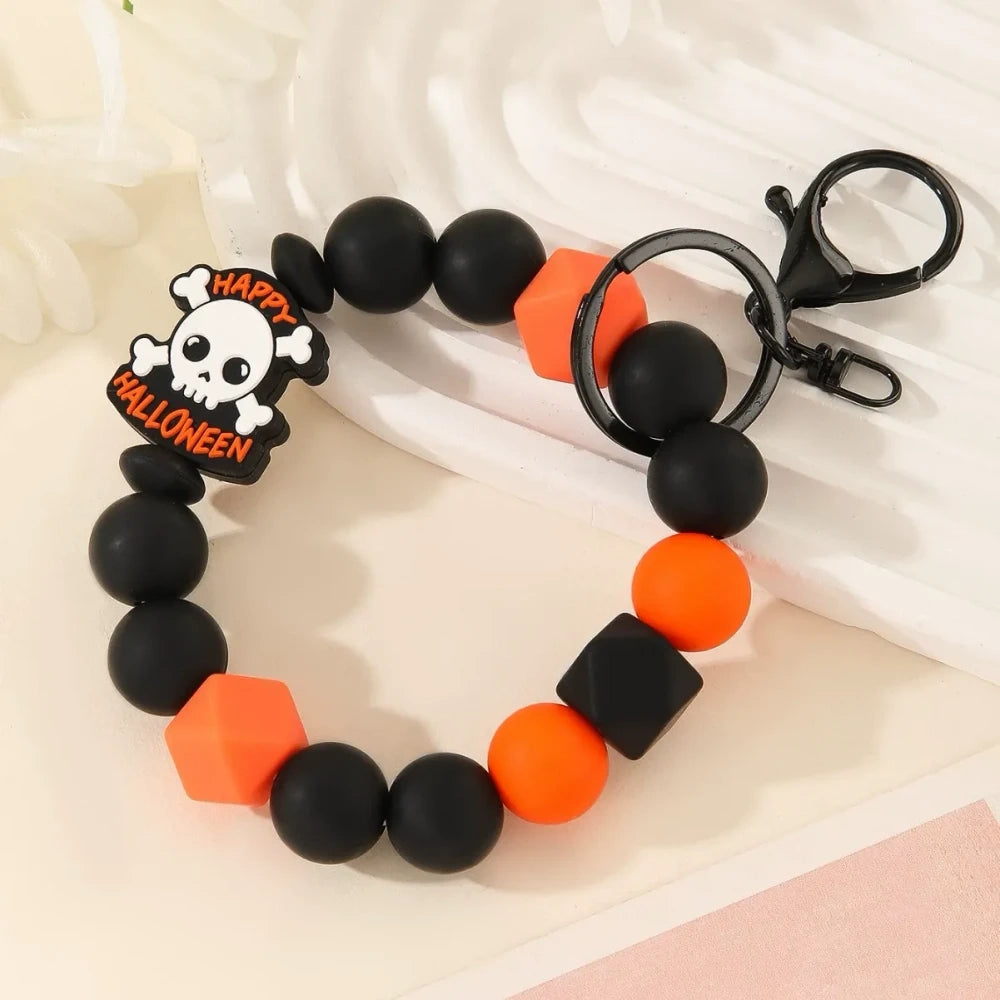 Halloween themed printed silicone beads in orange, black, yellow, purple and white featuring pumpkin, skull, ghost and Happy Halloween designs, shown as completed keychain bracelets and phone charms. - 2
