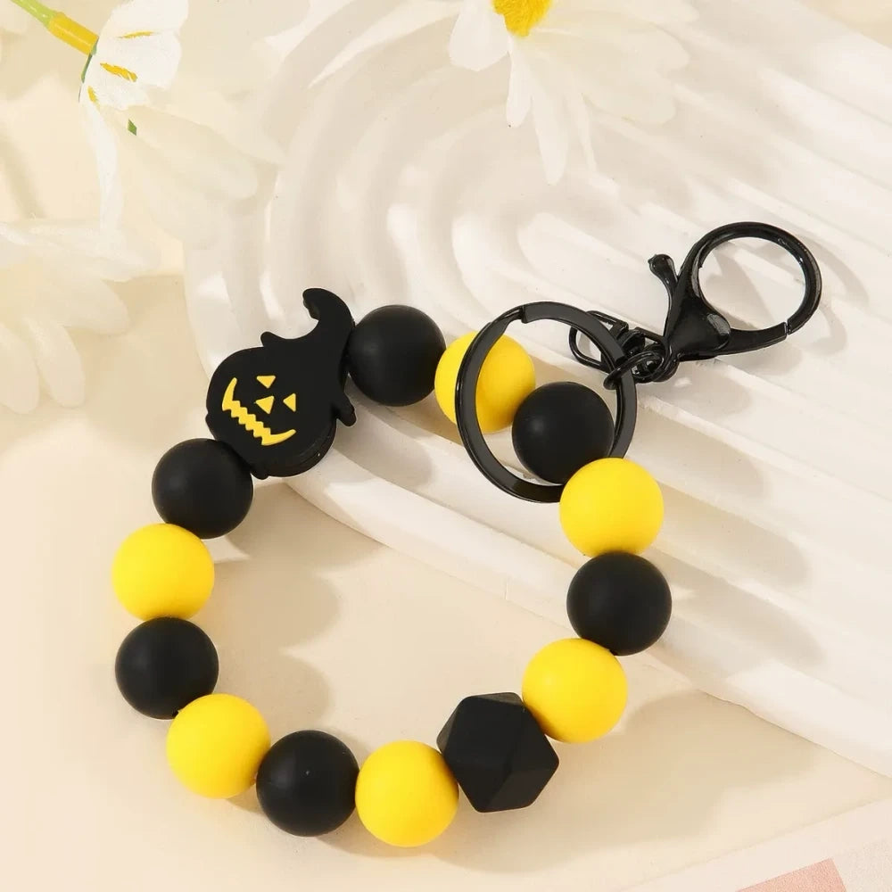 Halloween themed printed silicone beads in orange, black, yellow, purple and white featuring pumpkin, skull, ghost and Happy Halloween designs, shown as completed keychain bracelets and phone charms. - 3