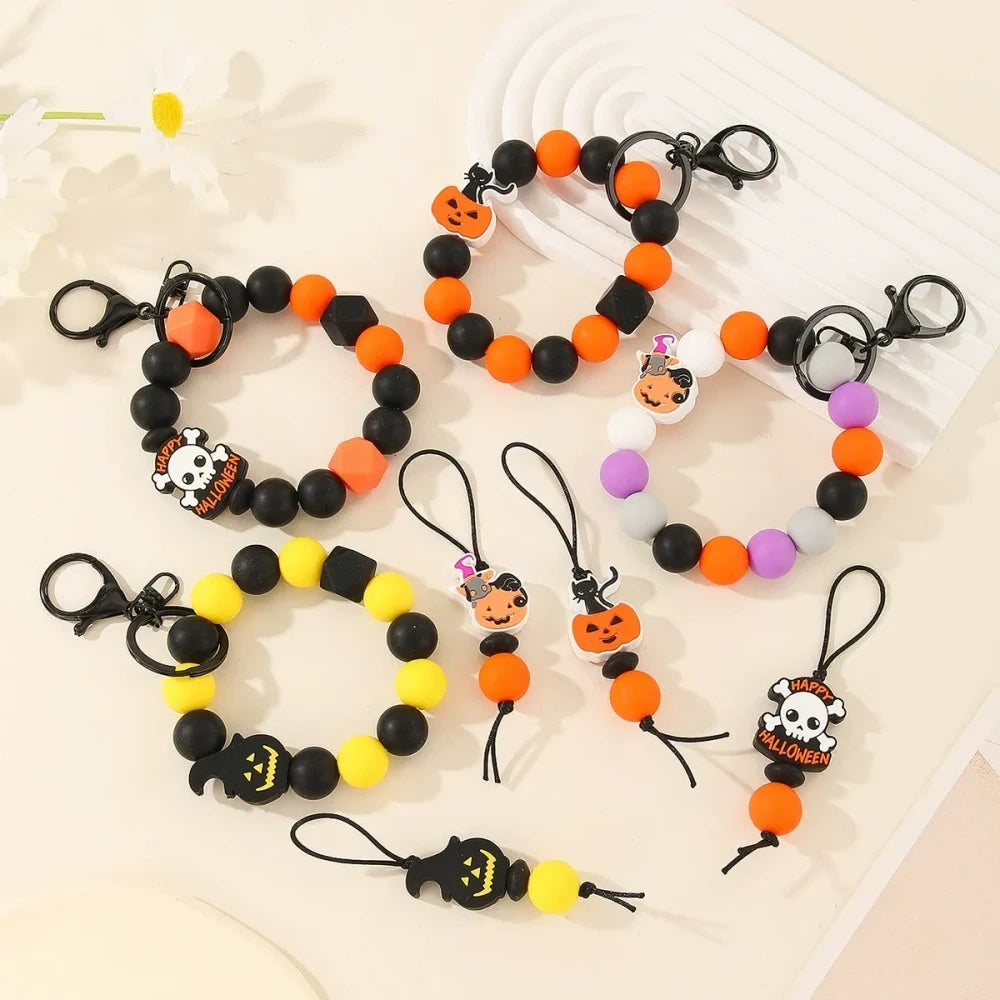 Halloween themed printed silicone beads in orange, black, yellow, purple and white featuring pumpkin, skull, ghost and Happy Halloween designs, shown as completed keychain bracelets and phone charms. - Random Mixed