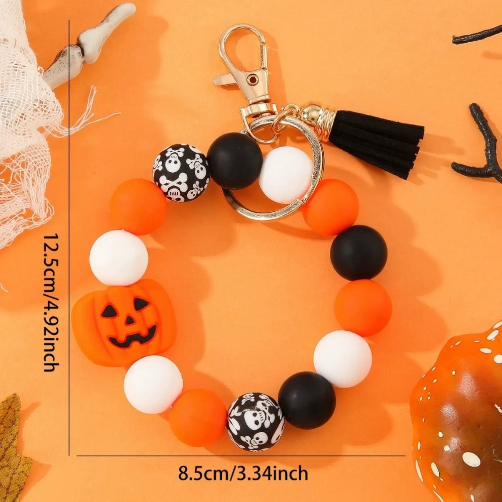 Halloween themed silicone beads in orange, black, and white with jack-o-lantern pumpkin and skull crossbones print beads arranged on a beaded keychain with black tassel and gold clasp on orange background
