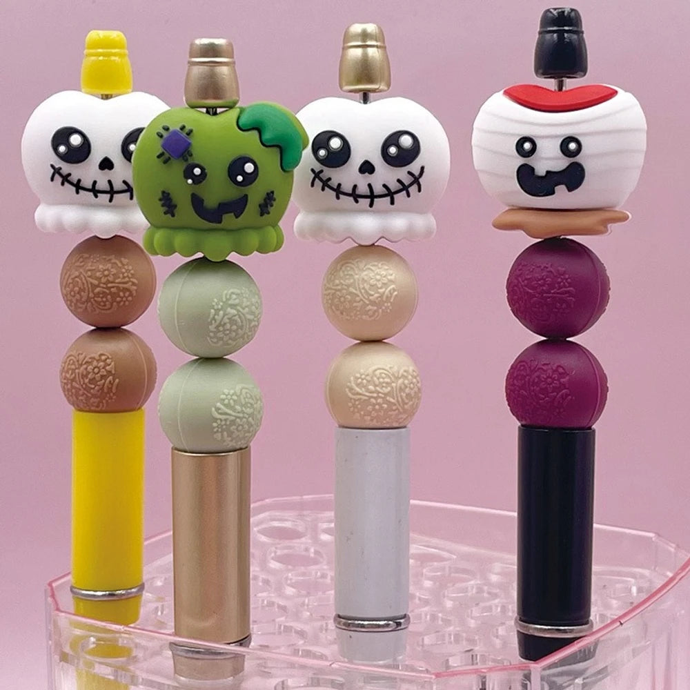 Halloween silicone 3D focal beads featuring skull and Frankenstein monster characters in white, green, and mummy designs, displayed on beadable pens with decorative round beads on a pink background.