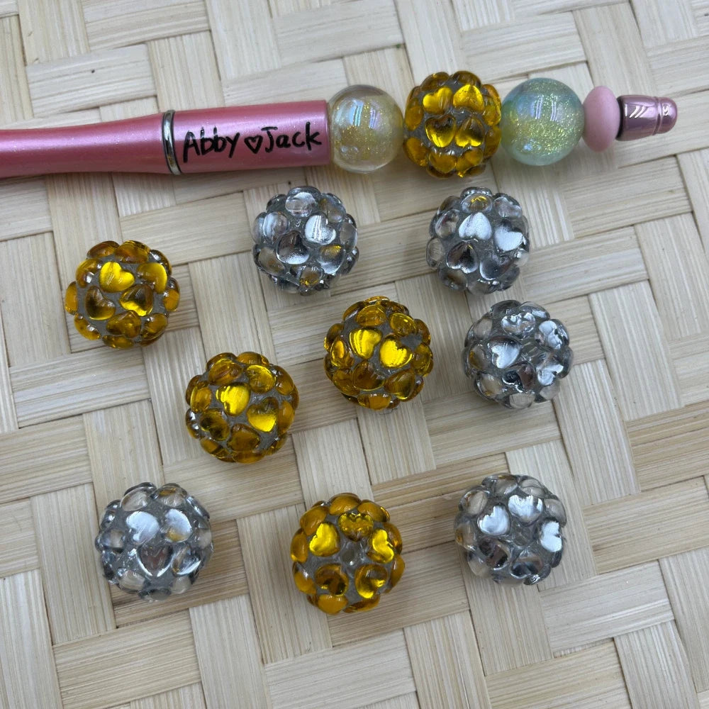 Gold and silver heart cluster bumpy acrylic fancy beads on woven bamboo surface next to a pink beadable pen labeled Abby and Jack