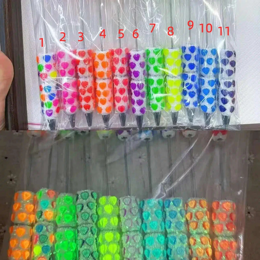 Set of 11 heart pattern rhinestone fuzzy beadable pens in neon multicolor designs shown in normal light and UV glow light, individually plastic wrapped