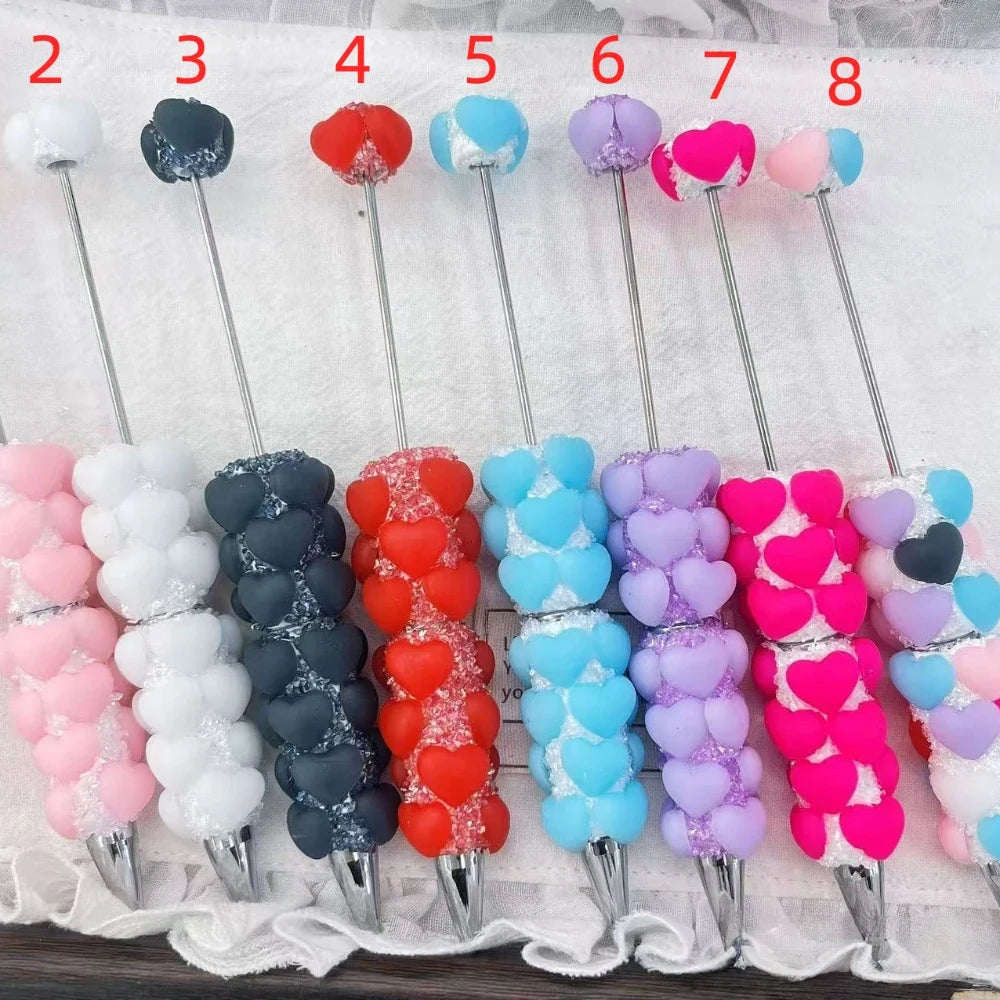 Seven heart-shaped rhinestone beadable pens in pink, black, red, blue, purple, hot pink, and multicolor with silver metal tips and needle tops, numbered 2 through 8.