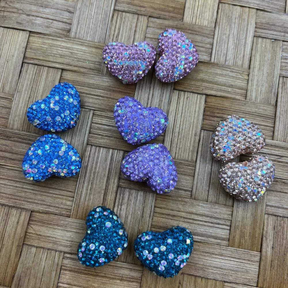 Heart shaped glitter rhinestone beads in pink, blue, purple, teal, and champagne colors displayed on a woven surface for DIY jewelry making and beadable pens.