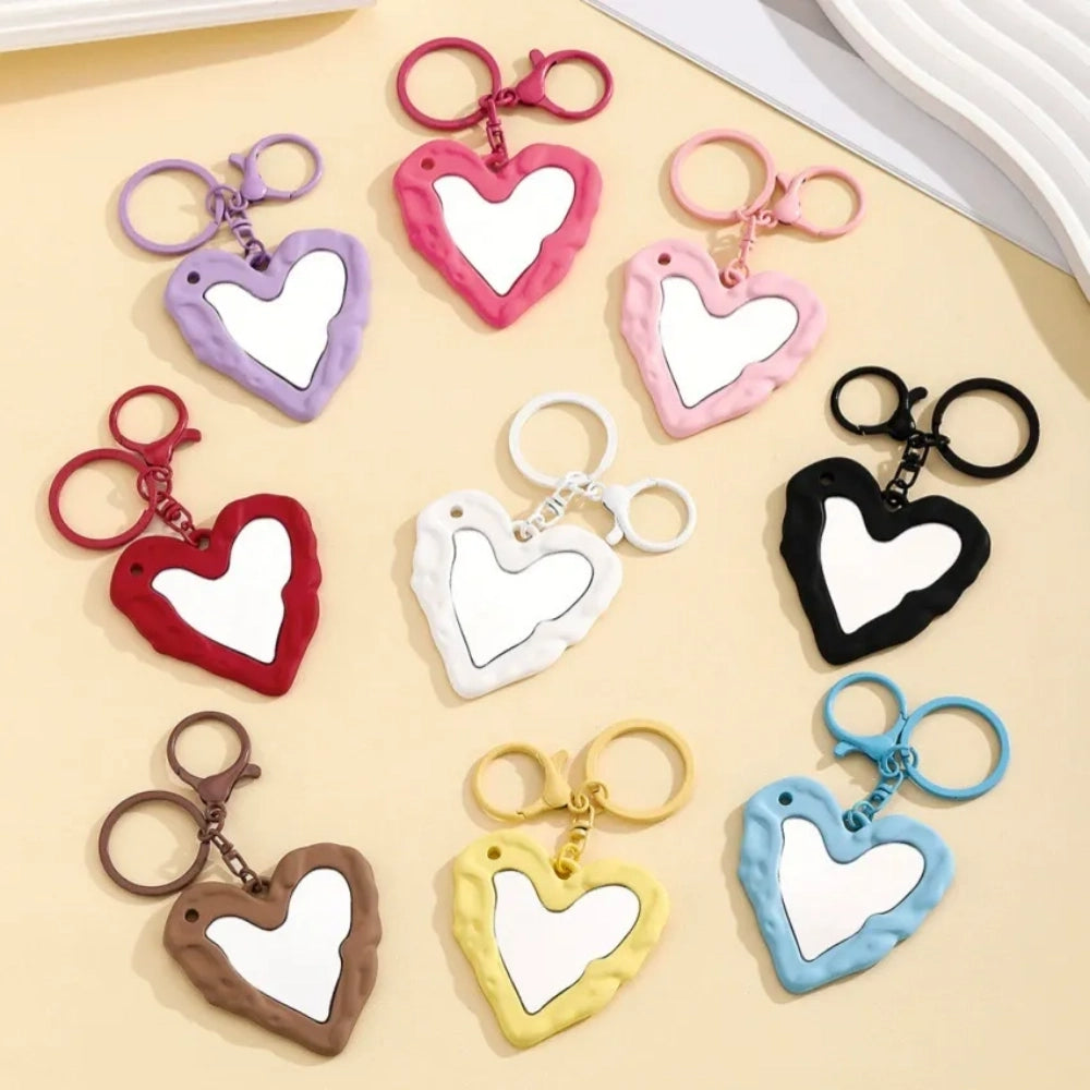 Nine colorful heart-shaped photo frame keychain pendants in purple, pink, hot pink, red, white, black, brown, yellow, and blue with lobster clasp rings on a beige surface.